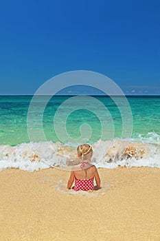 Girl sitting in the ocean breaking waves on the sand beach