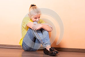 Girl sitting offended on the floor, light orange background