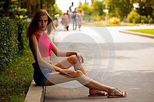 Girl sitting in the Park with the edge of the road on the curb