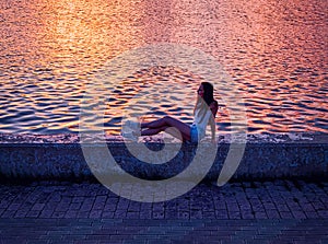 Girl sitting on pier and looking at the river side view sunset time