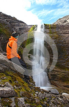 Girl sitting on a rock and looking at the beautiful waterfall