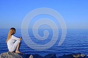 Girl sitting on the rock by the peaceful sea