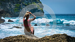 Girl sitting on the Rock and watching Huge Waves hitting Tembeling Coastline at Nusa Penida Island, Bali Indonesia