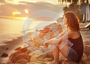 Girl sitting on the rocks on the beach and watching the sunset