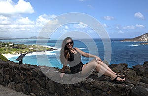 A girl sitting on a rocks a front of the ocean bay