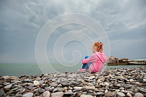 Girl sitting on a rocky beach with knees