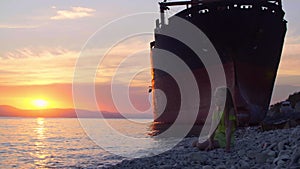 Girl sitting on sea coast and throwing pebbles during sunset