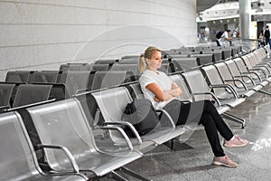 The girl is sitting on the seat at the airport alone. Flight delay