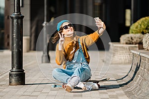 Girl sitting on skateboard and use mobile phone. Outdoors, urban lifestyle. cute skater girl sitting on skate board checking smart