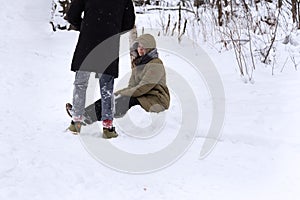 The girl is sitting in the snow and waiting for the guy to help her get up.