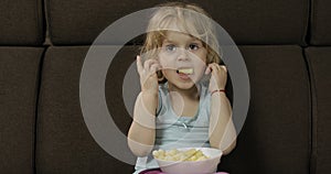 Girl sitting on sofa and eating corn puffs. Child taste puffcorns