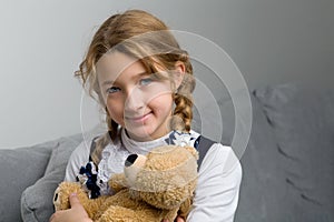 Girl sitting on sofa hugging teddy bear