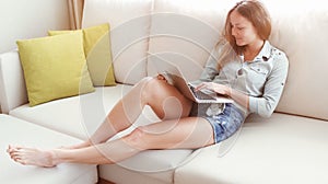 Girl sitting in a sofa and typing something on her laptop. Young woman using the laptop at the sun set.