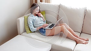 Girl sitting in a sofa and typing something on her laptop. Young woman using the laptop at the sun set.