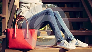 Girl sitting on the stairs with a big red super fashionable handbags in a sweater jeans and sneakers on a warm summer evening. War