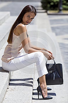 girl sitting on the stairs in chic shoes with a stylish black bag