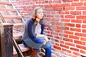 Girl Sitting on Stairway, Next to Red Brick Wall