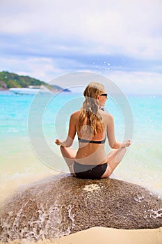 Girl sitting on stone backward near sea