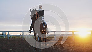 Girl Sitting Straight On The Back Of A Dark Bay Horse In The Sandy Arena - Sunset