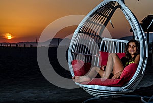 Girl sitting in the swing on the beach in the sunset