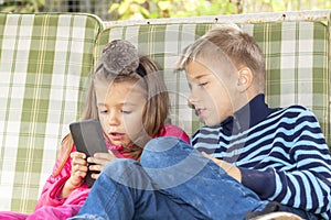 Girl is sitting on swing and playing mobile games on smart phone. boy sits next to her and worries about process of playing friend
