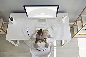 Girl sitting at table with computer, watching online lesson and typing homework at home