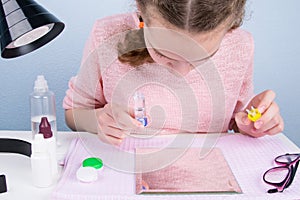 The girl is sitting at the table, looking in the mirror at the eyes and changing contact lenses to improve vision