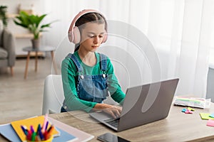 Girl sitting at table using laptop, wearing headset