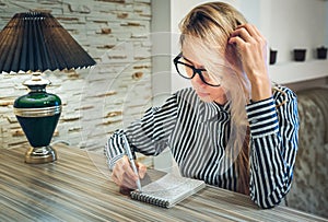 Girl sitting at the table and writes in a paper notebook amounts