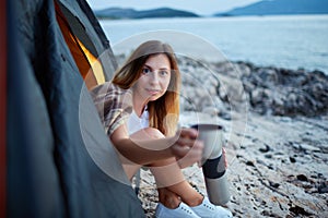 Girl sitting in tent, stretching cup of tea offering to drink.