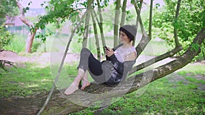 Girl sitting on a tree, smiling, using the phone