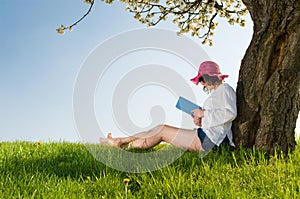 Girl sitting under a blossom tree reads a book