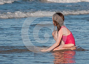 Girl sitting in the water from the beach and looking out to sea