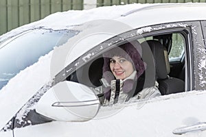 A girl is sitting in a white car while driving. Winter, day.