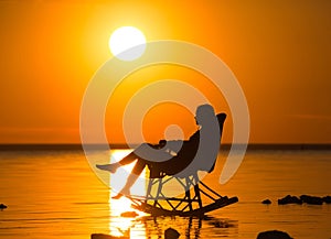 A girl sitting in a wicker rocking chair against the sunset