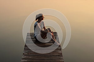 Girl sitting on a wooden pier or jetty on the lake at sunset