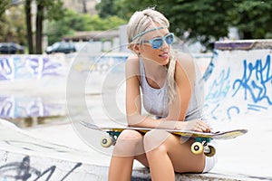 Girl with skateboard sitting in skatepark