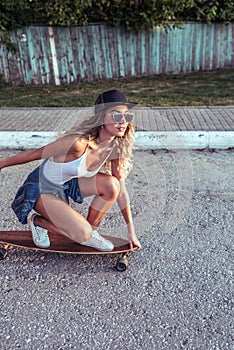 Girl on a skateboard, in summer in city, white body, jacket, jeans, black baseball cap, sunglasses. On the background of