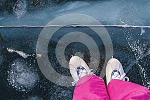 A girl skater in vintage skates and pink ski pants skates on the beautiful fairy blue clear ice of Lake Baikal with cracks.