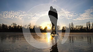 Girl skating on frozen river during beautiful sunset. Young woman shod in figure skates sliding on ice. Shining sun is