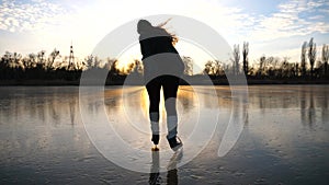 Girl skating on frozen river during beautiful sunset. Young woman shod in figure skates sliding on ice. Shining sun is