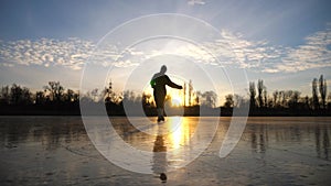 Girl skating on frozen river during beautiful sunset. Young woman shod in figure skates sliding on ice. Shining sun is