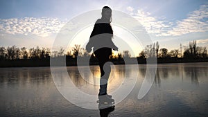 Girl skating on frozen river during beautiful sunset. Young woman shod in figure skates sliding on ice. Shining sun is