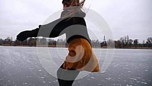 Girl skating on frozen river or lake at cloudy day. Young woman shod in figure skates sliding on ice rink at nature