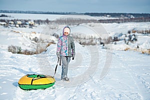 Girl in ski clothes drags tubing snow on the hill