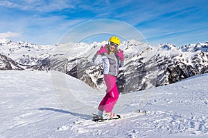 Girl skier in grey jacket and pink pants on a slope rides