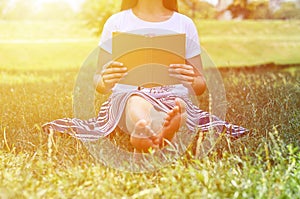 Girl in skirt sitting on the grass in the Park and reading a book. Concept of learning and leisure