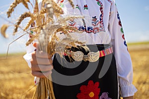 Girl slavic in traditional ethnic folklore costume with Bulgarian embroidery standing on a harvest golden wheat field