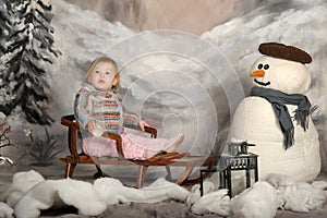Girl on a sled next to a snowman