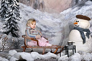 Girl on a sled next to a snowman